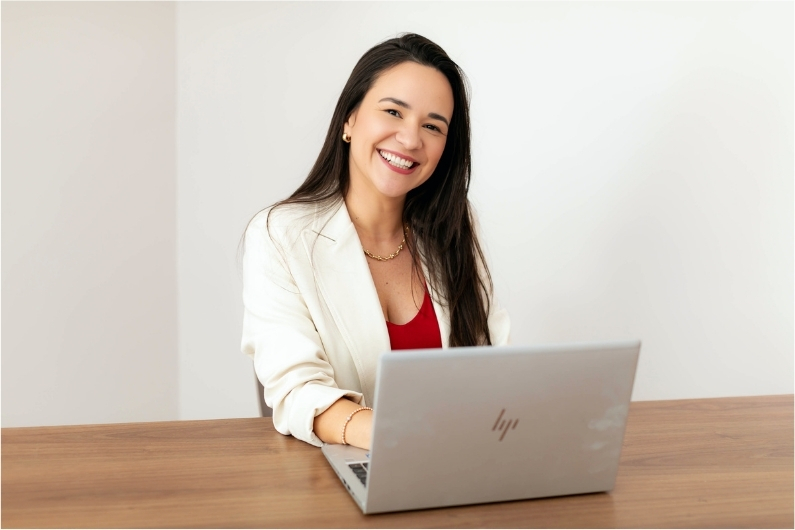 Tai Senra sorrindo à mesa com seu computador